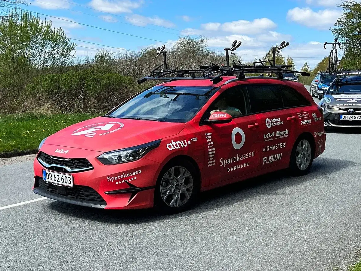 Red team car of Team Aalborg-Sparekassen Danmark on the road with bike racks on the roof