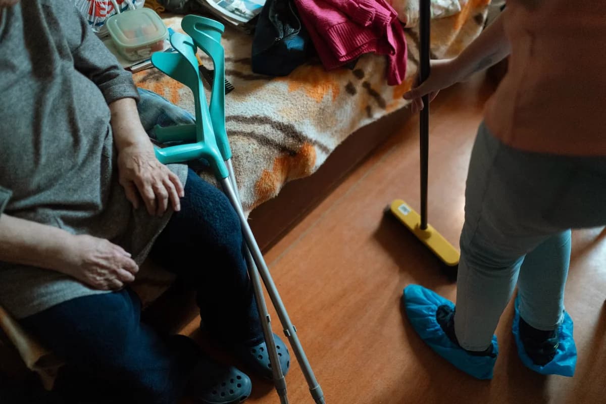 A care worker helps an elderly woman clean in her home.