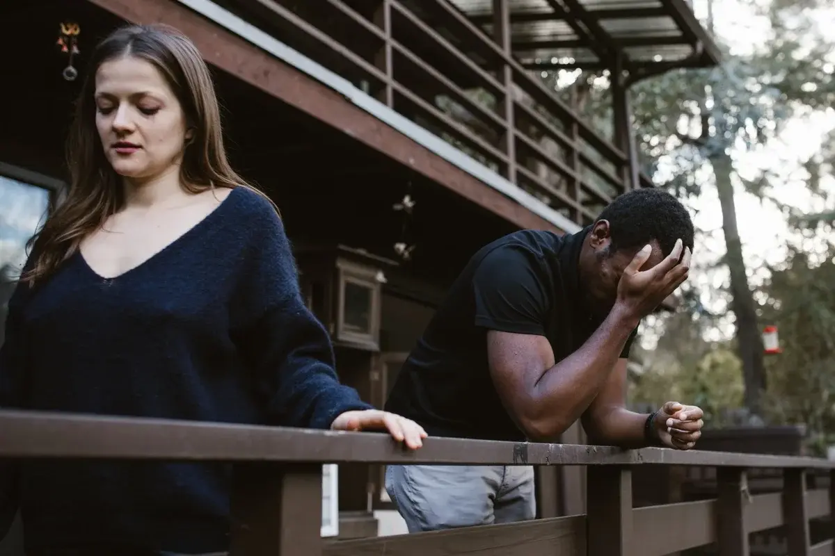 A woman and a man stand on a wooden deck looking upset.