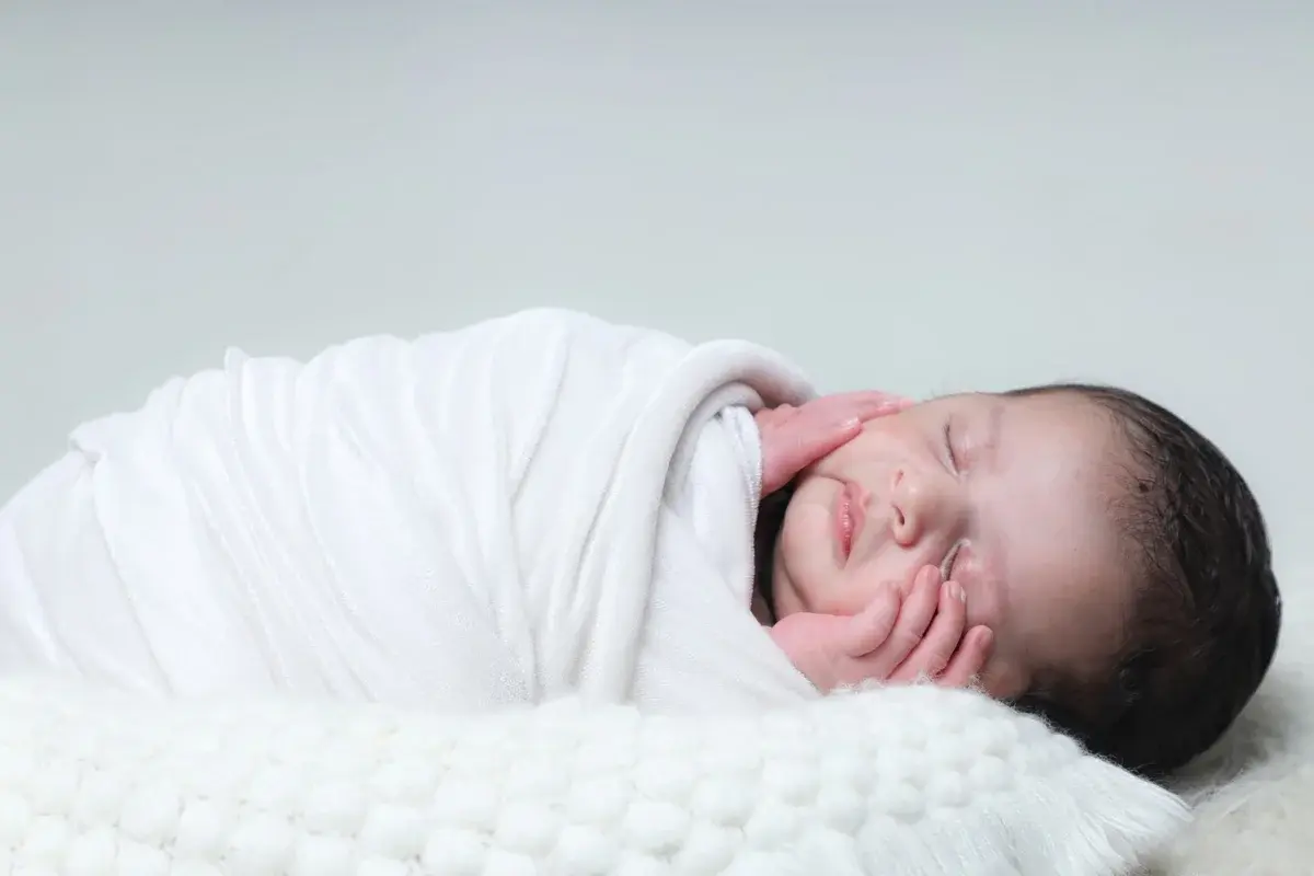 A sleeping newborn baby wrapped in a white blanket.