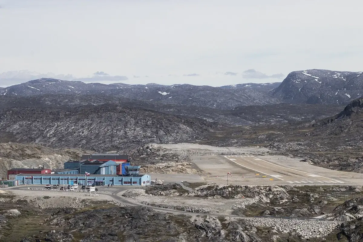 Wide view of Ilulissat Airport with runway and terminal buildings in a rocky Arctic landscape.