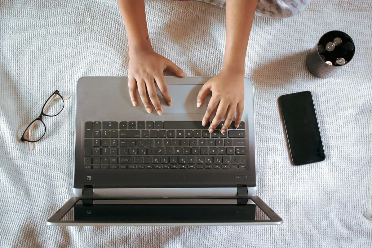 Top-down view of a laptop with hands typing, plus glasses and a smartphone.