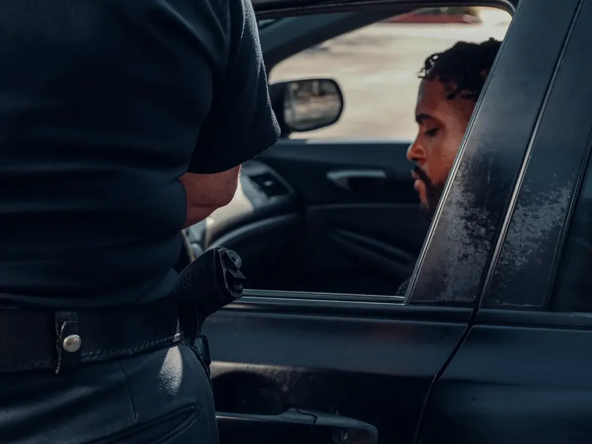 A police officer talks to a man seated in a black car with the window down.