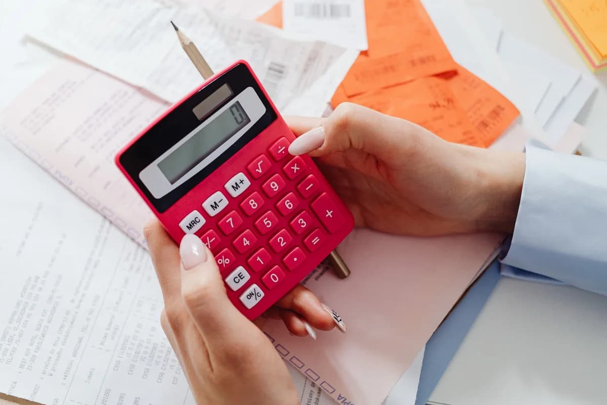 Hands holding a red calculator over paperwork and receipts