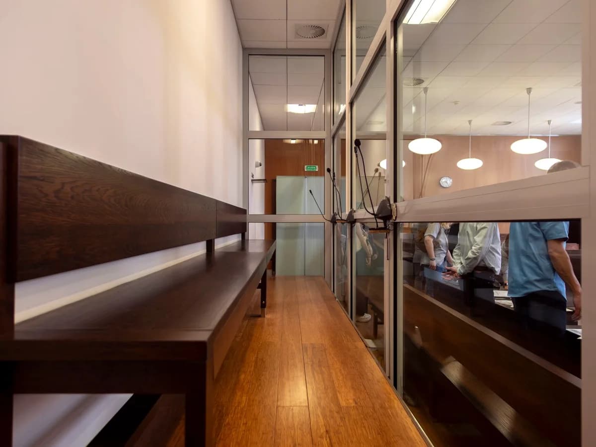 A modern courtroom interior with wooden benches, glass partitions, and microphones.