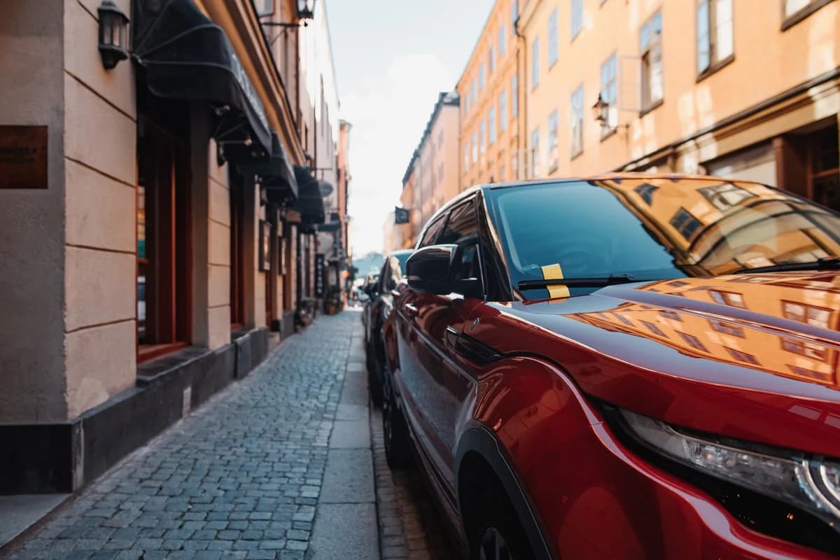 Red car parked on cobblestone street with buildings