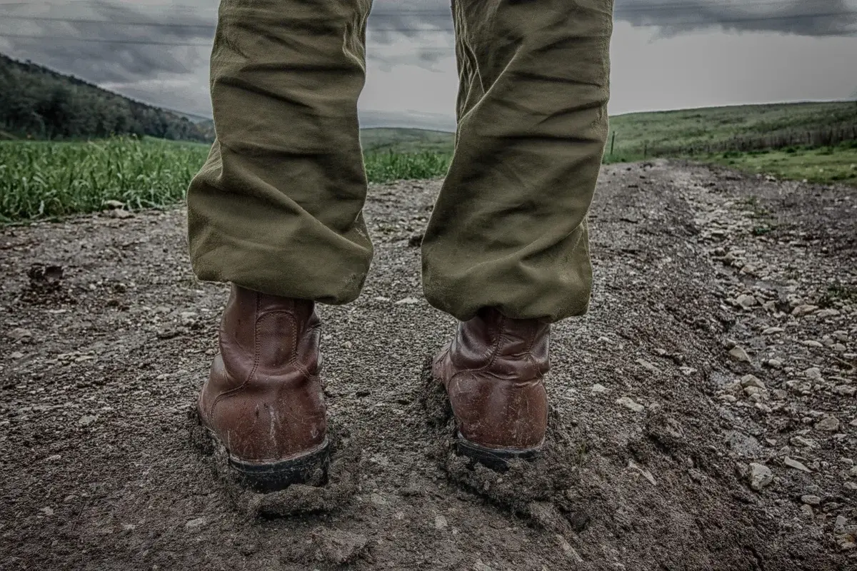 Close-up of military boots standing on a muddy road.