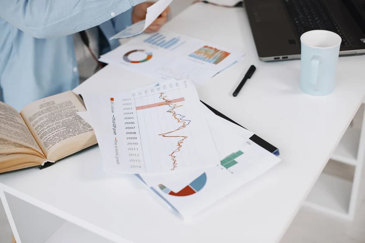 White office desk with a laptop, open book, printed charts, and a mug.
