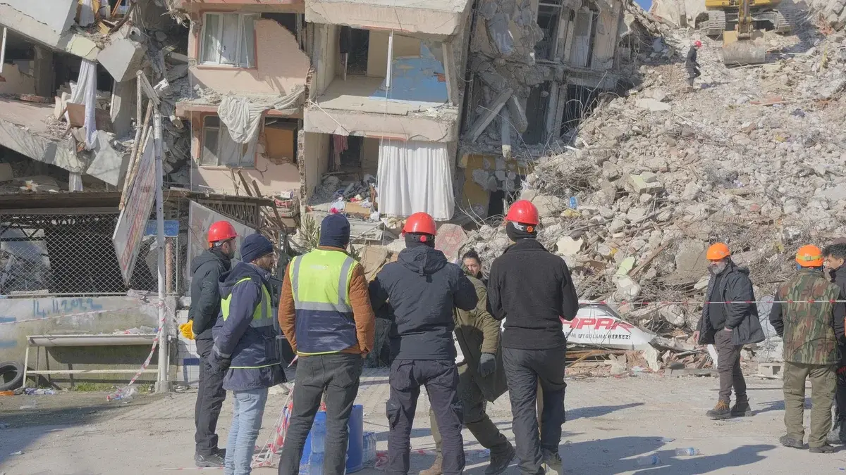 Rescue workers in helmets surveying earthquake ruins
