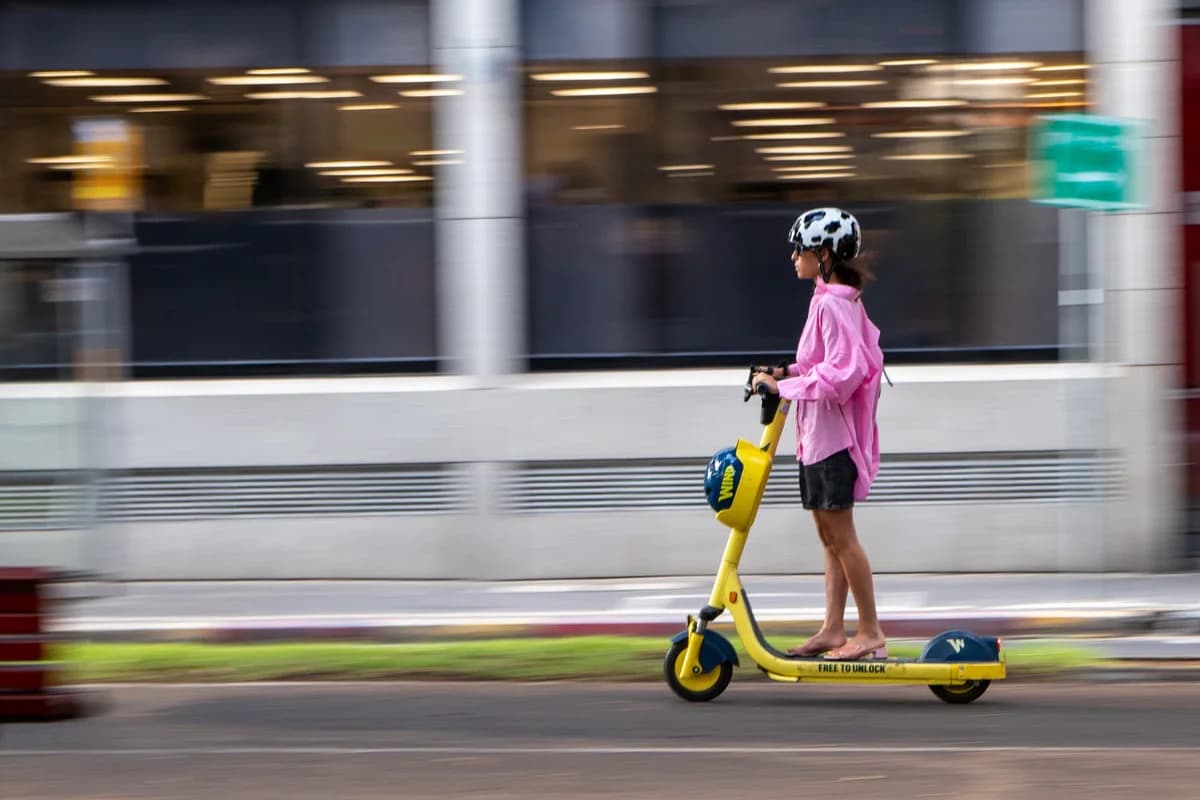 Woman in a pink jacket riding a yellow electric scooter on a city street