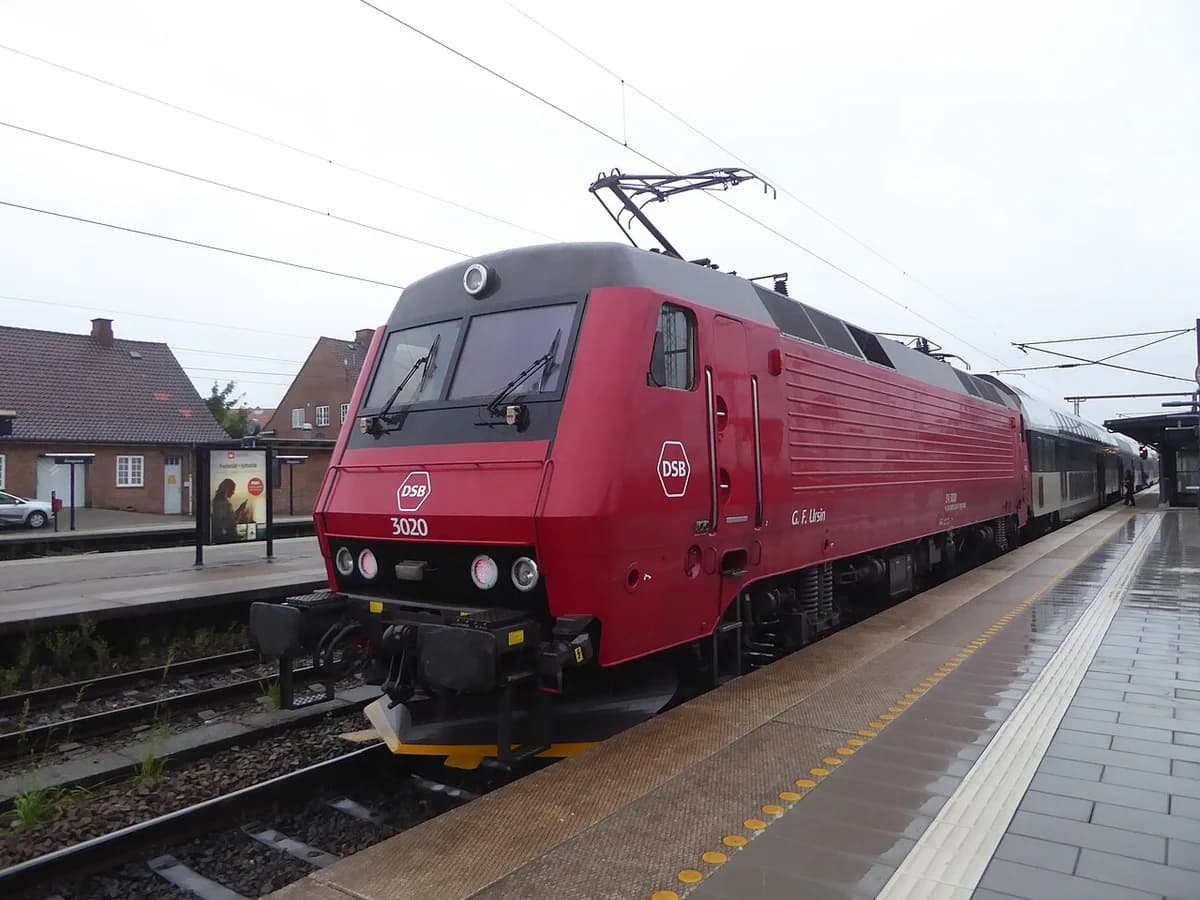 A red electric locomotive at a Danish train station platform.