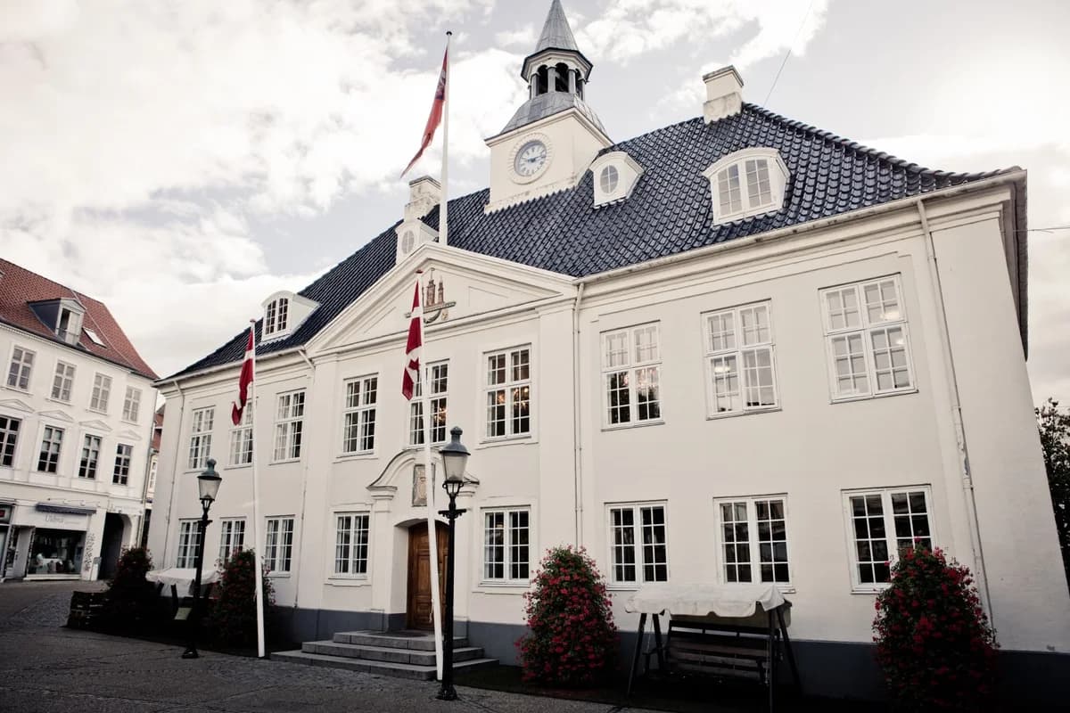 White historic town hall building with Danish flags in a town square.