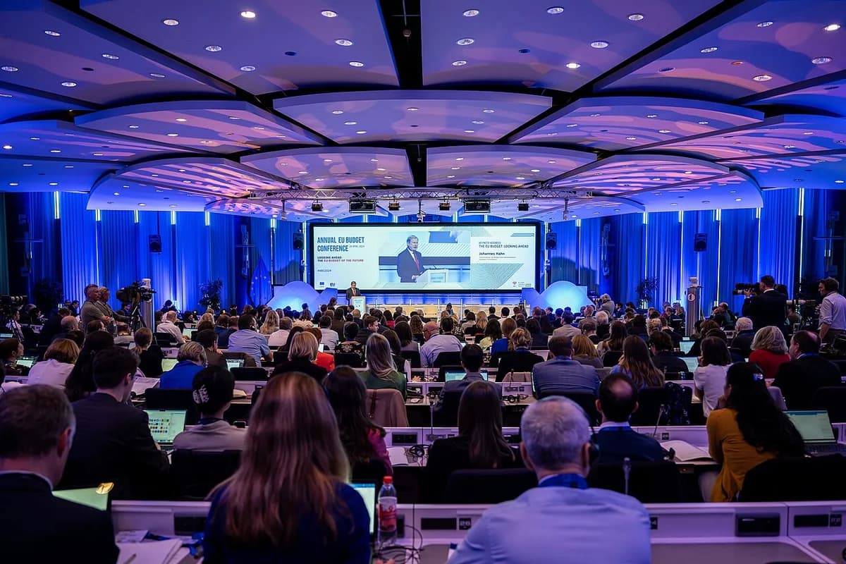 Wide shot of attendees in a conference hall watching a speaker on stage at an EU budget conference.