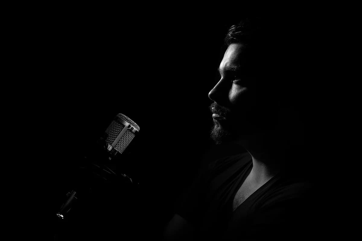 Black-and-white profile of a man speaking into a microphone in a studio.