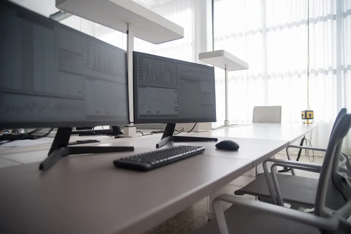 Modern office desk with multiple computer monitors and ergonomic chairs.
