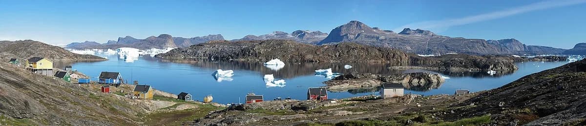 Panorama of a small Greenlandic settlement with houses, water, icebergs, and mountains.