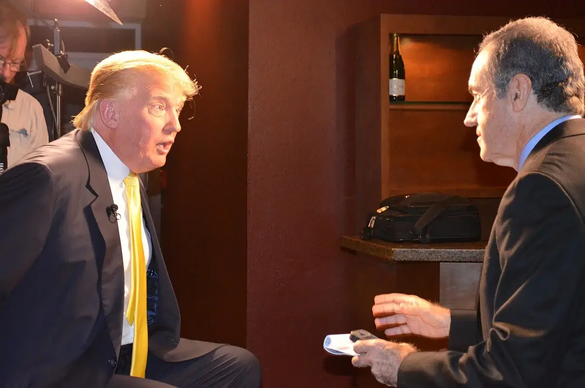 Donald Trump speaking with a man during an indoor interview.