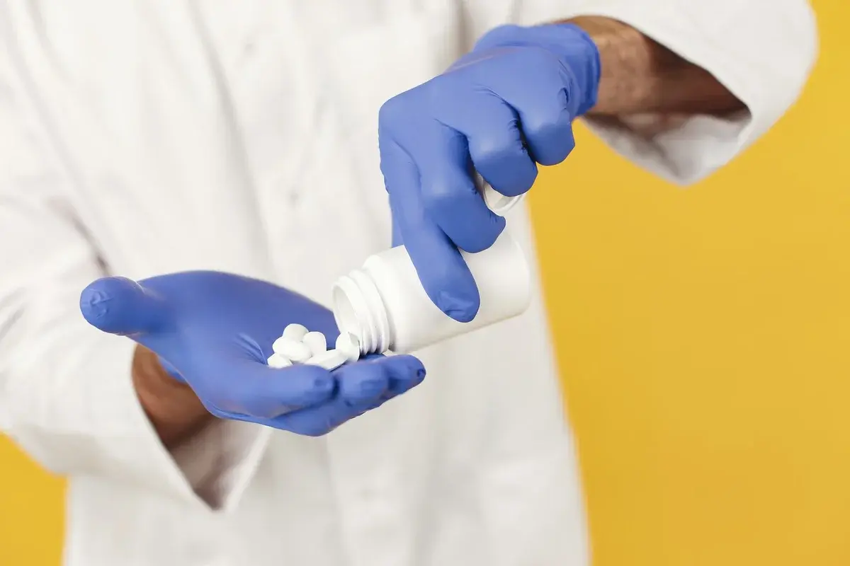 Gloved hands pouring pills from a bottle