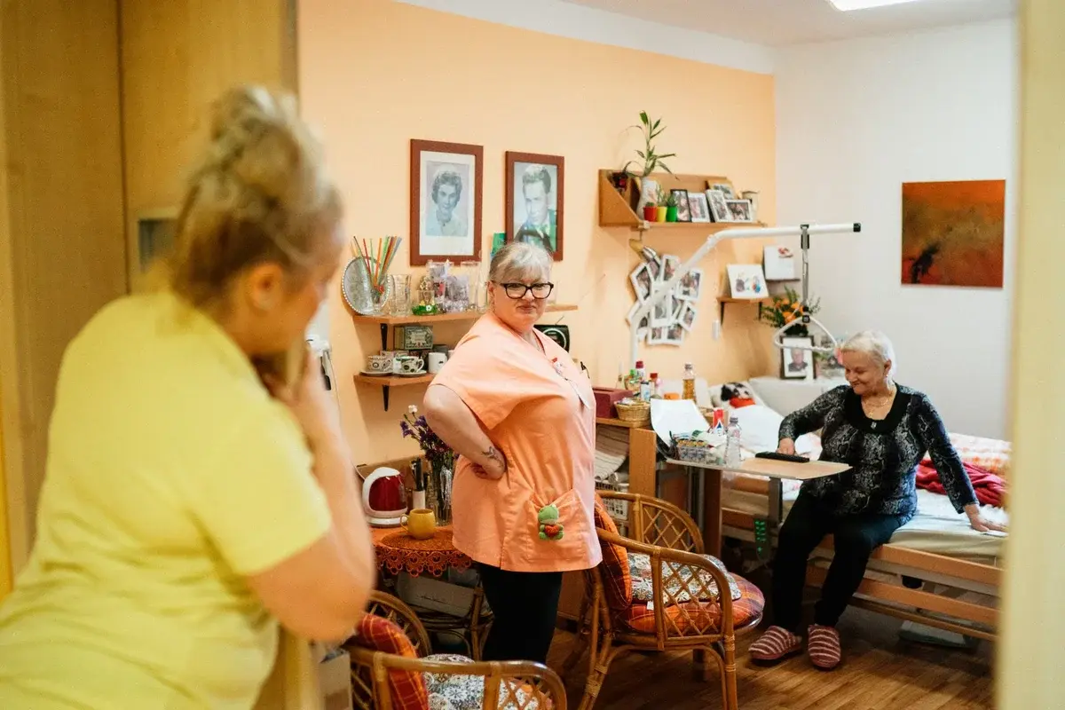 Caregiver talking with an elderly woman in a cozy care home room.