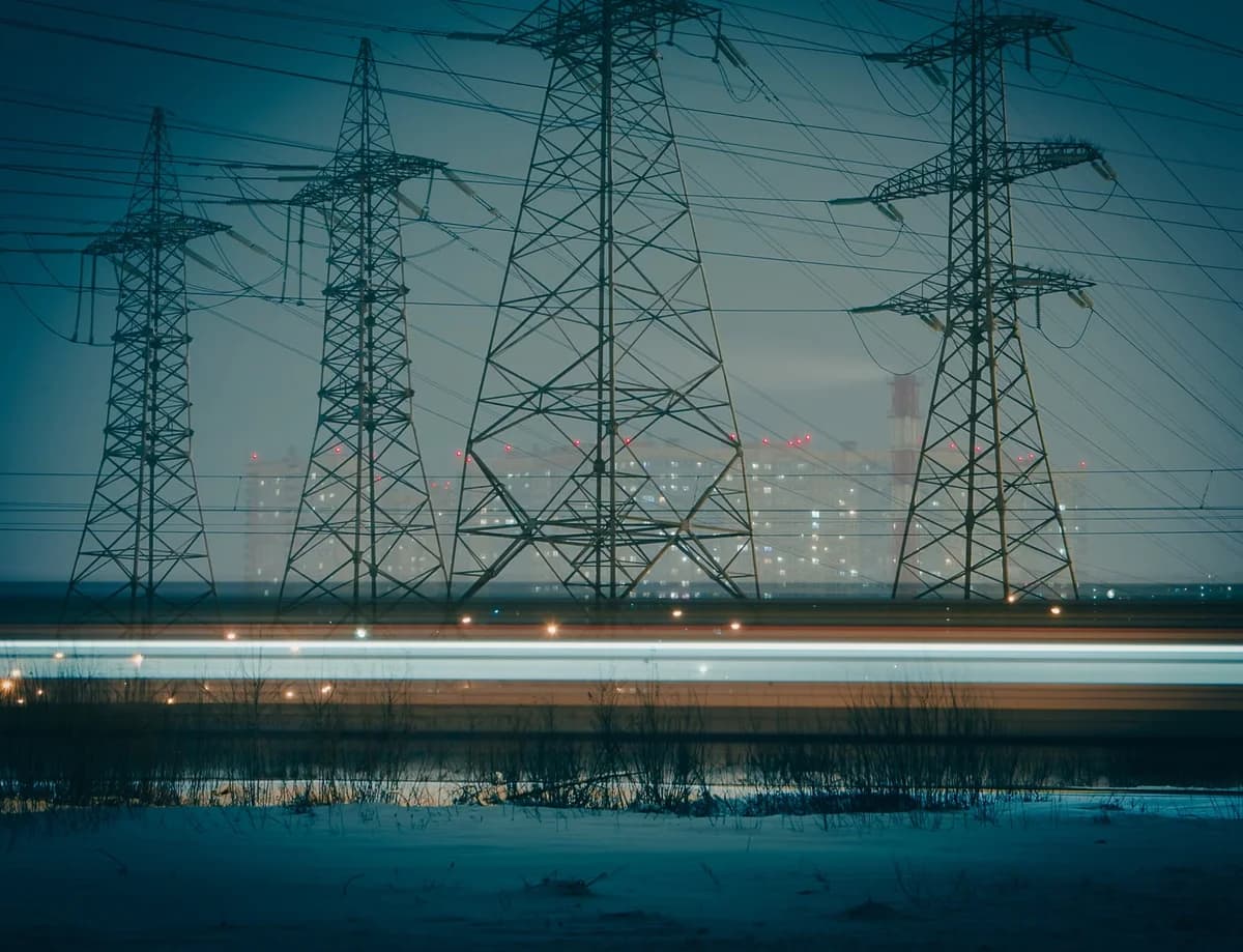 High-voltage power towers silhouetted against a city at night.