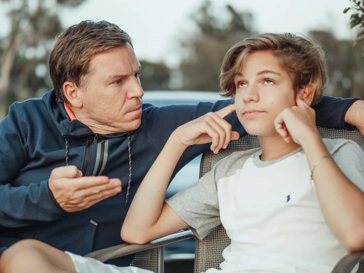 Father frustrated talking to teenage son who covers ears outdoors
