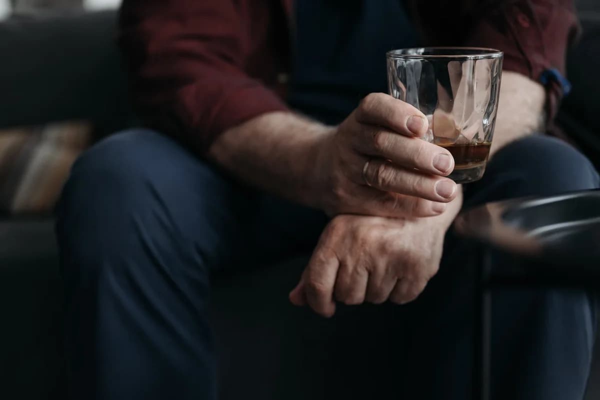 A close-up of a hand holding a whiskey glass indoors.