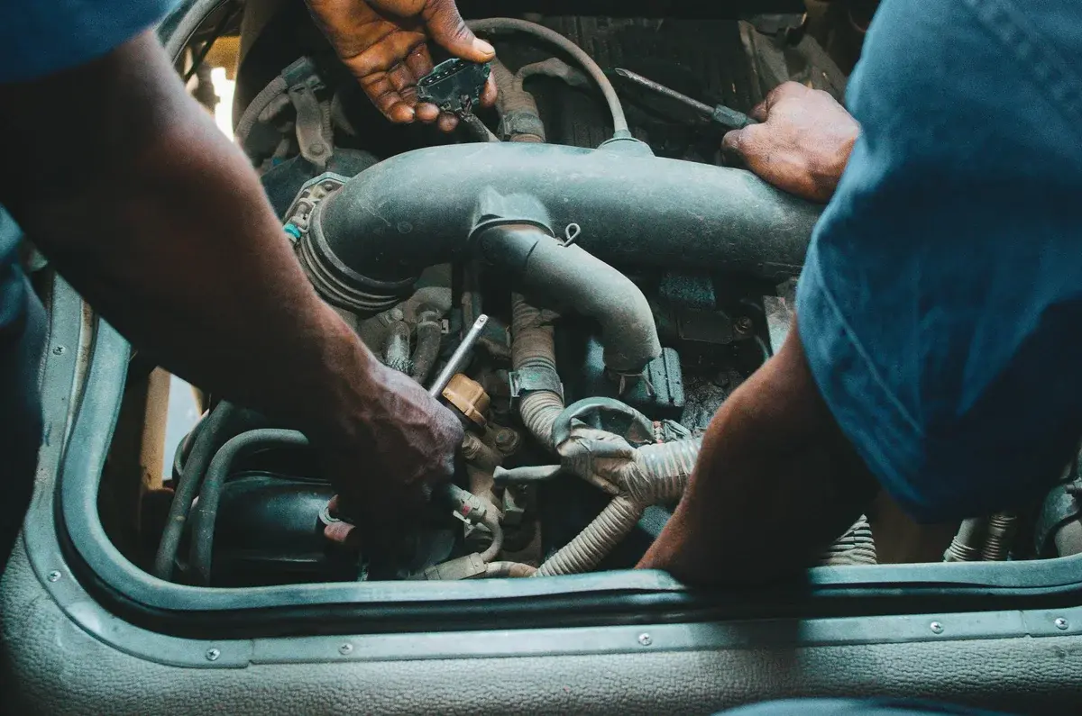 Two mechanics working on a car engine with tools.