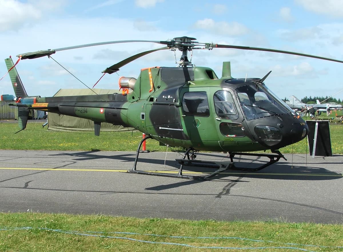A green military helicopter parked on a tarmac at an airfield