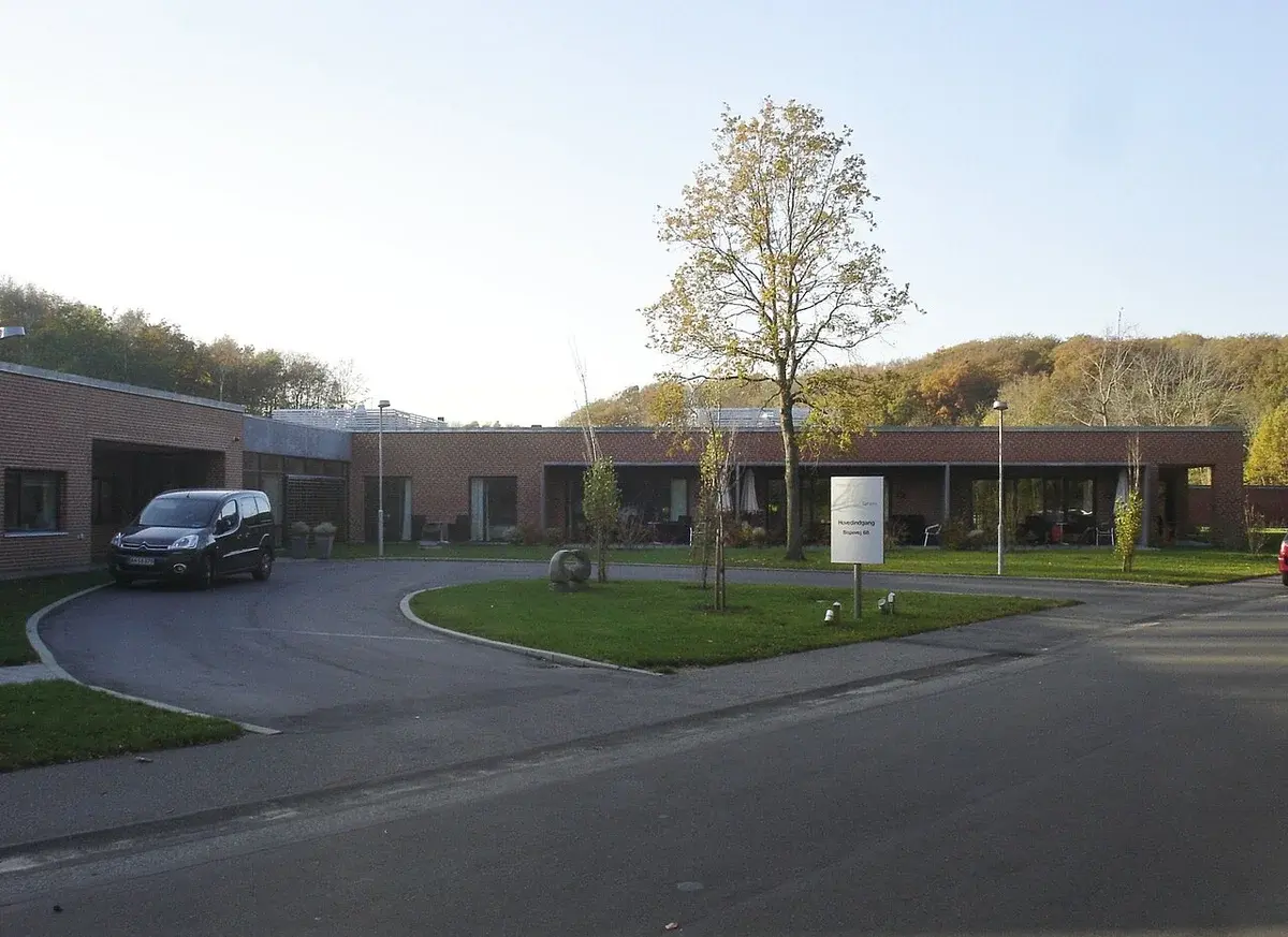 A modern brick hospice building with a driveway and trees in front.