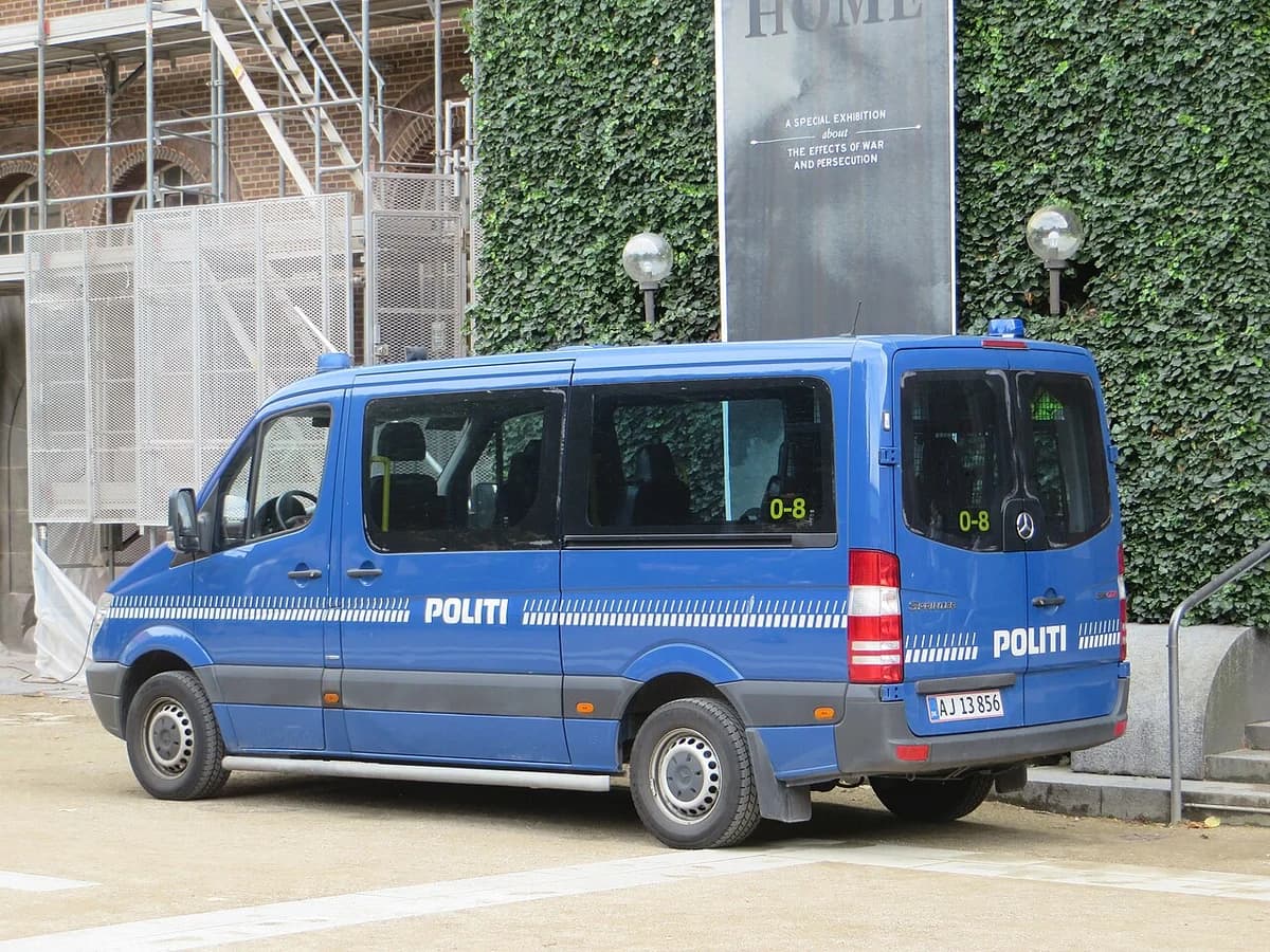 A blue Danish police van marked POLITI parked beside an ivy-covered building with scaffolding.