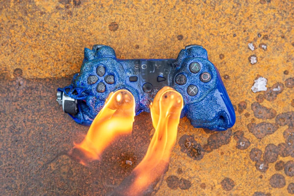 A blue game controller melting in flames on a rusty surface.