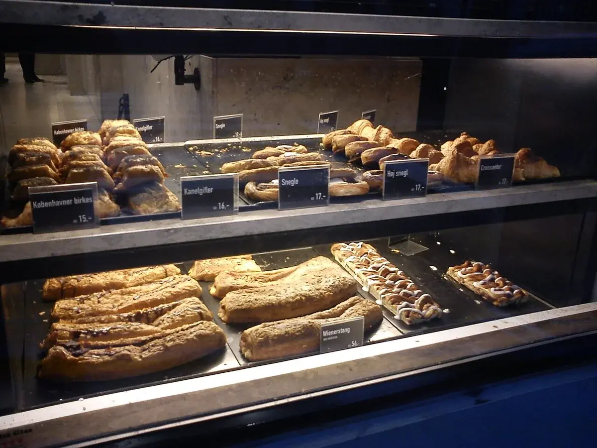 Bakery display case with assorted Danish pastries and price labels.