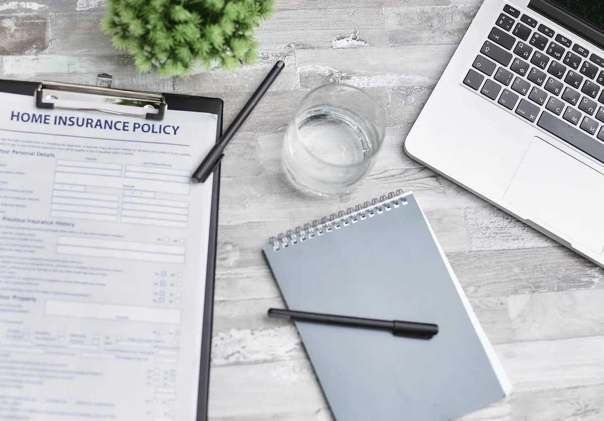 Flat lay of a home insurance policy with a laptop and notebook on a desk.