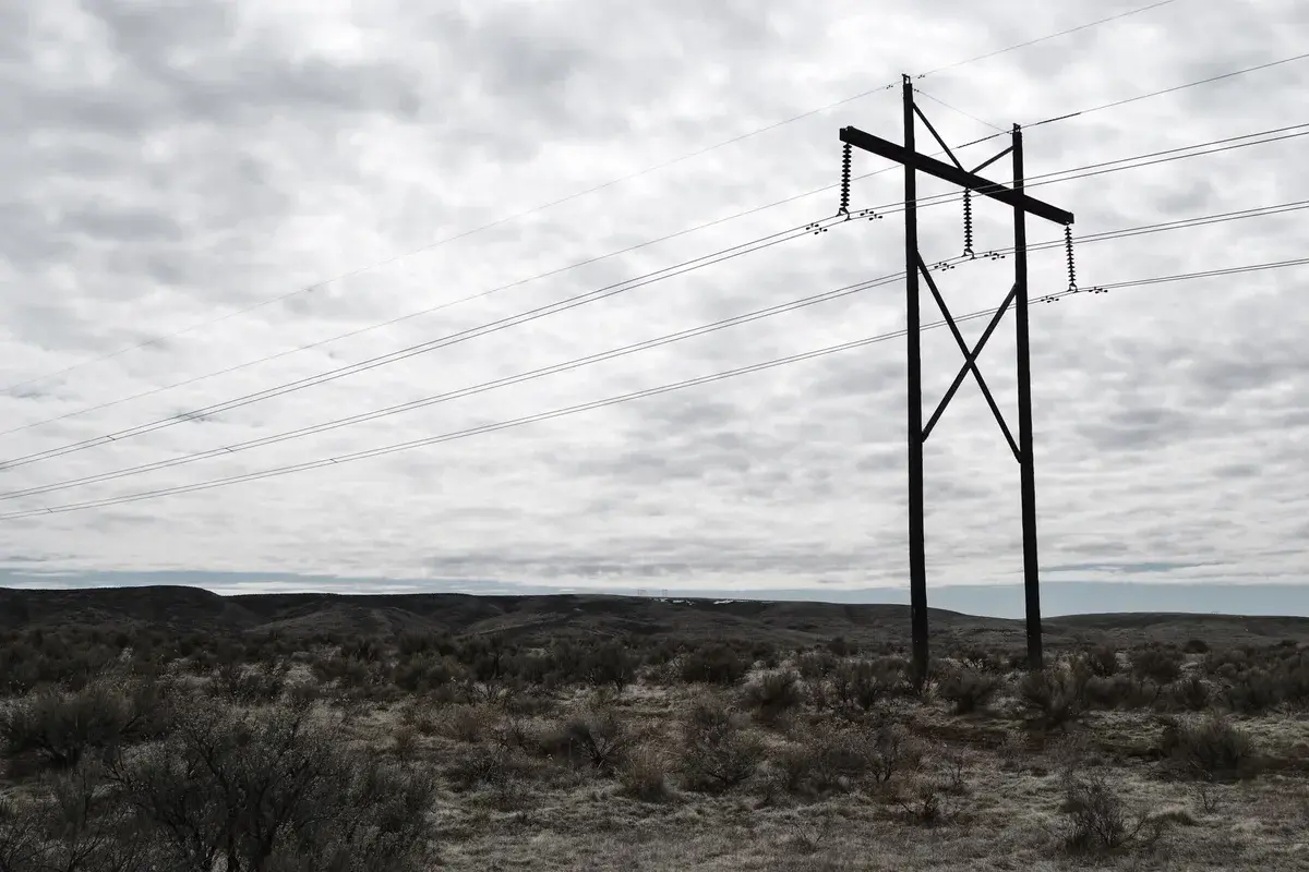 Power lines crossing a barren landscape under a cloudy sky.