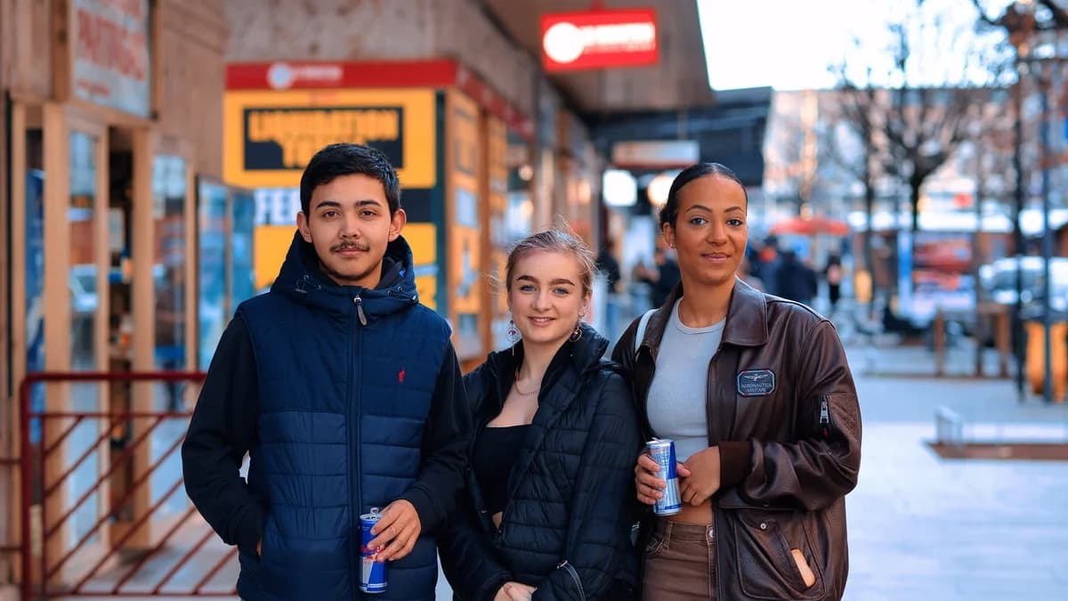 Three young adults holding energy drinks on a city street.