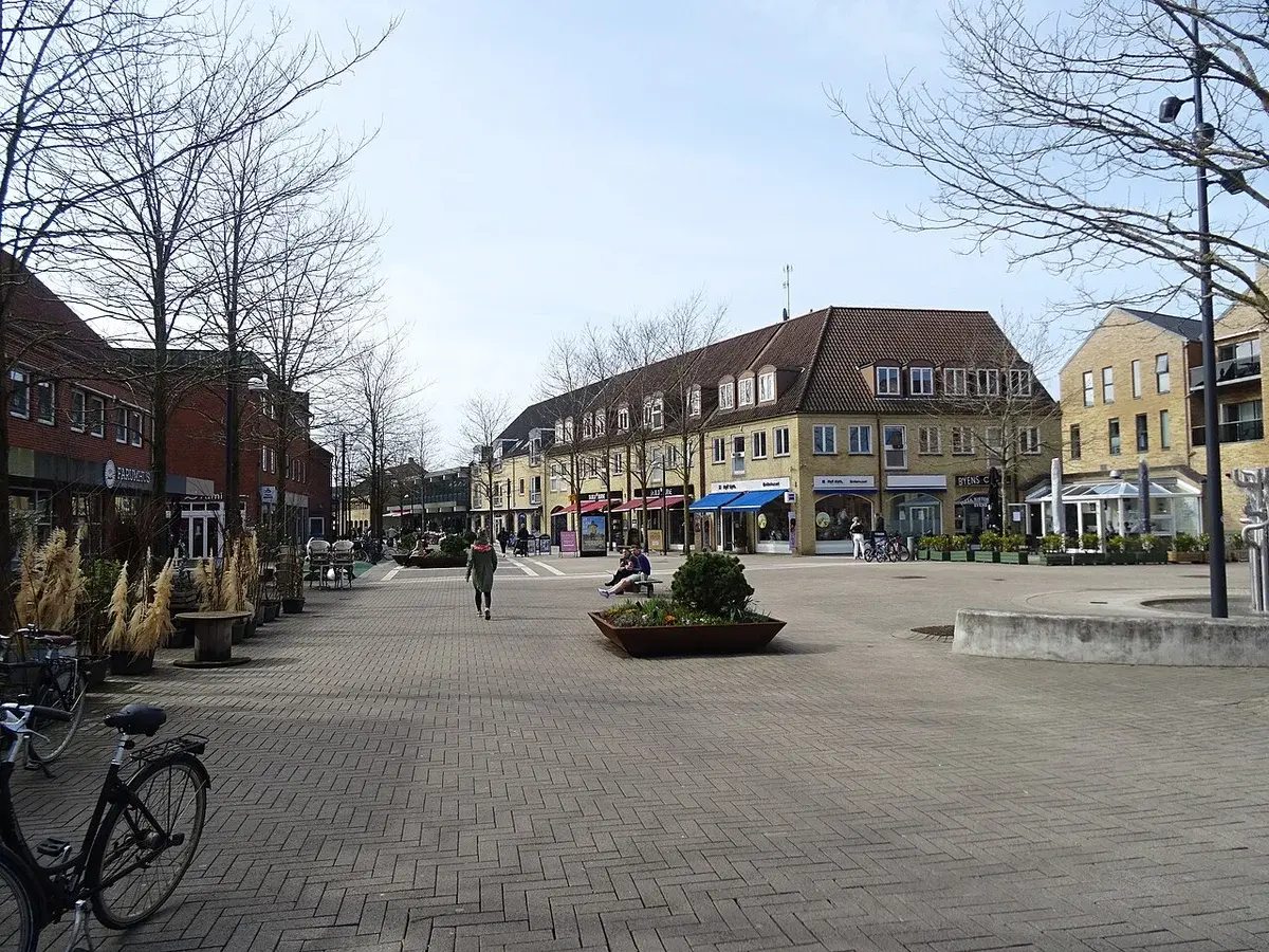 Pedestrian street with shops, trees, and a few people in Lillerød, Denmark.