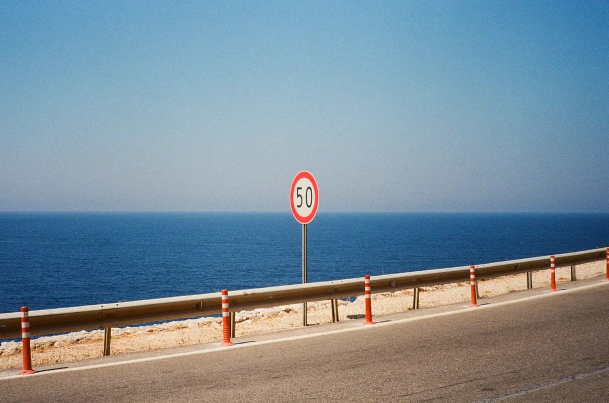 A coastal road with a 50 km/h speed limit sign overlooking the sea.
