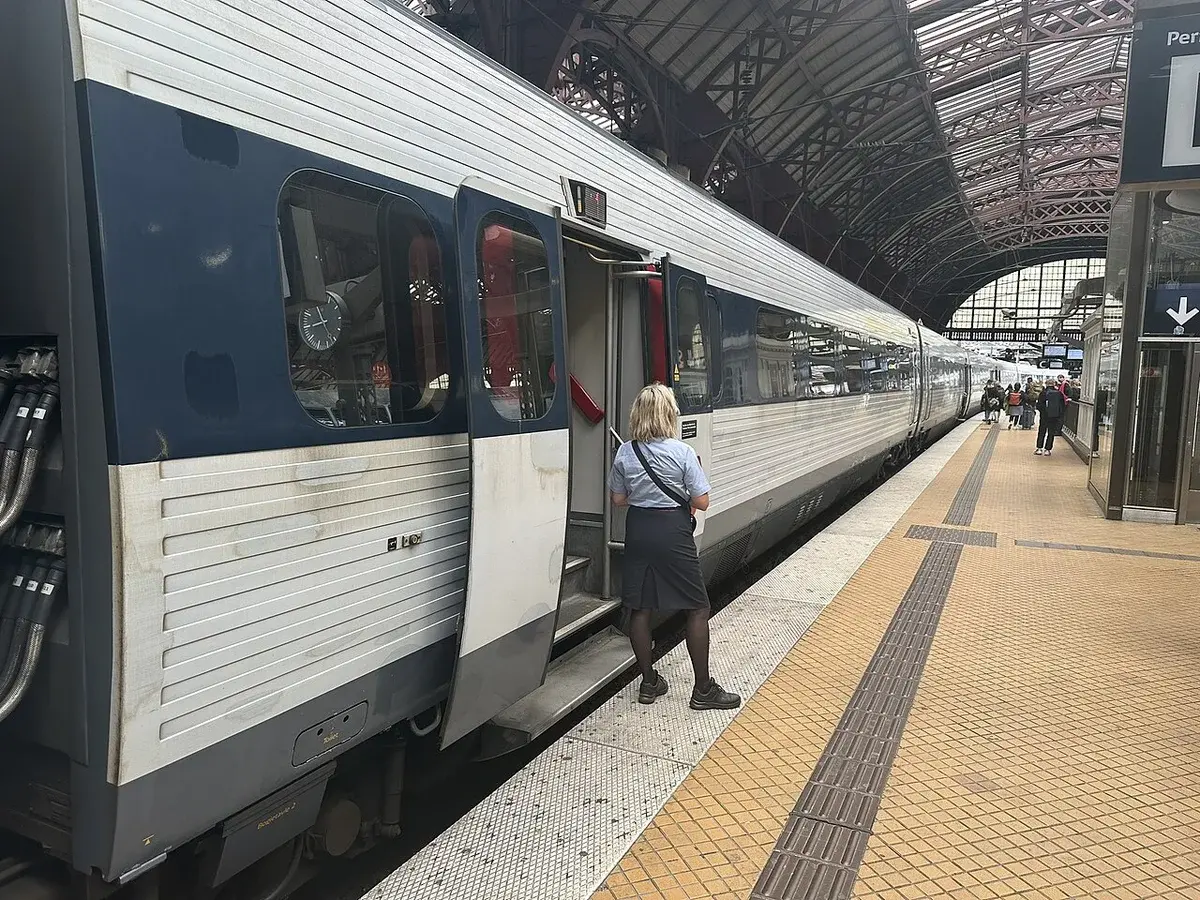 A DSB IC3 train stopped at a platform at Copenhagen Central Station with a conductor standing nearby.