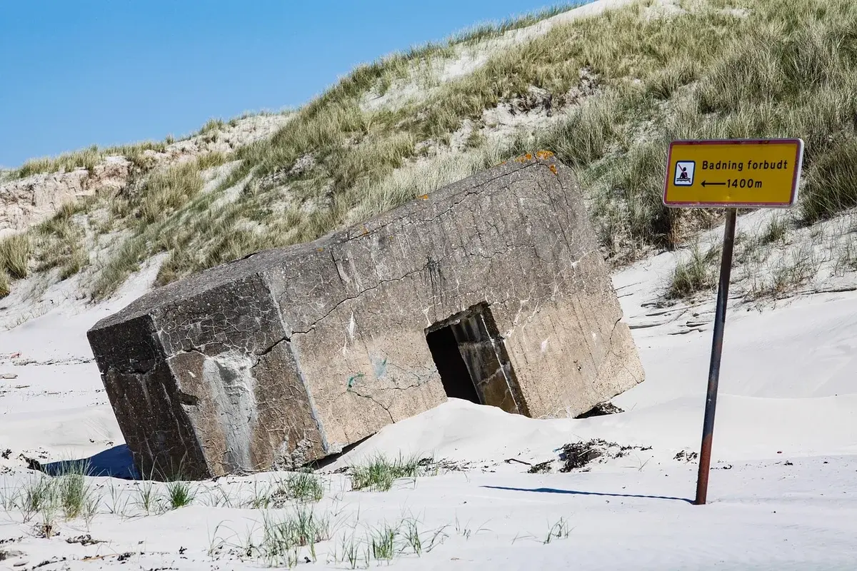 A partly buried concrete bunker in sandy dunes with a bathing forbidden sign.