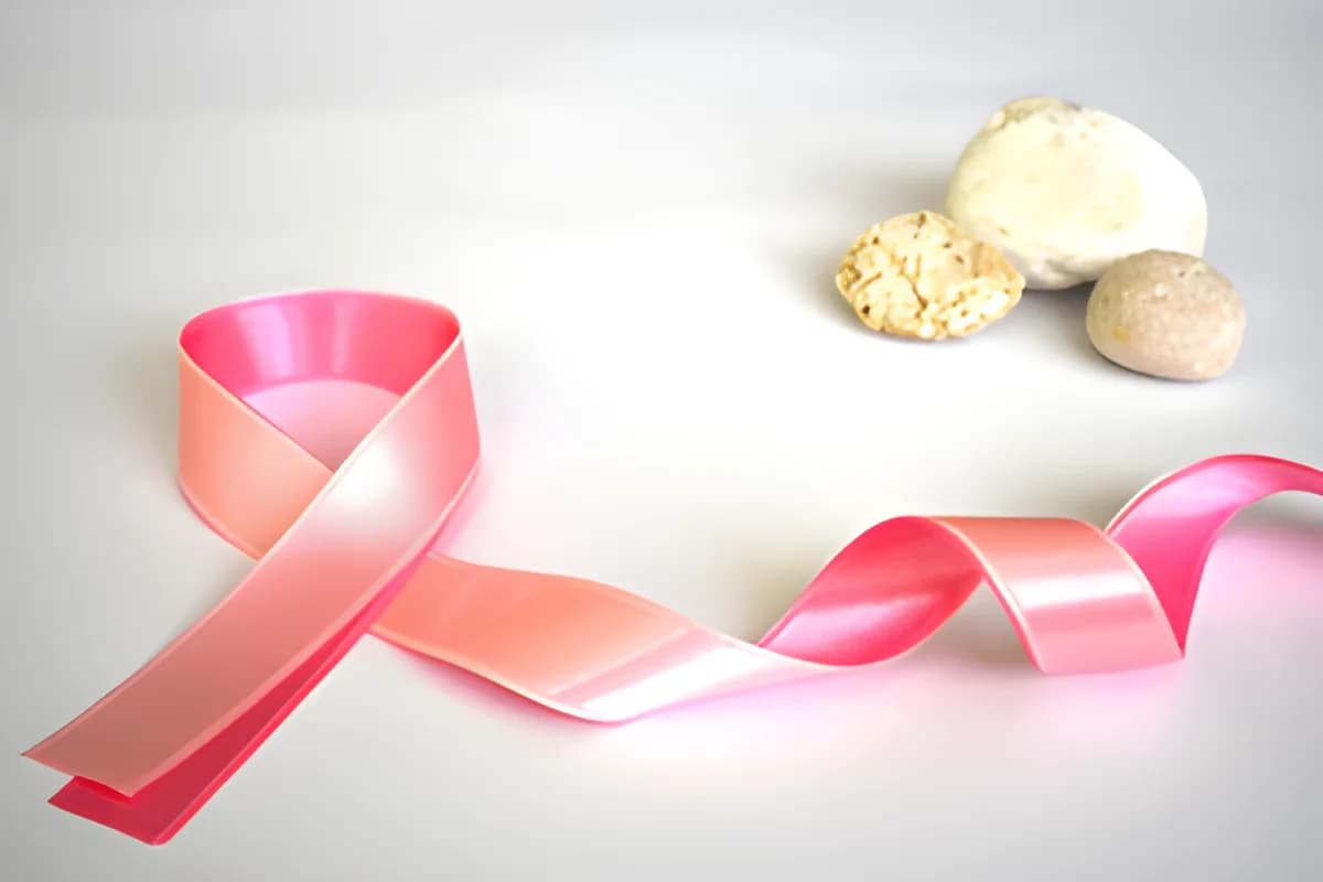 Pink breast cancer awareness ribbon beside three small stones on a white background.