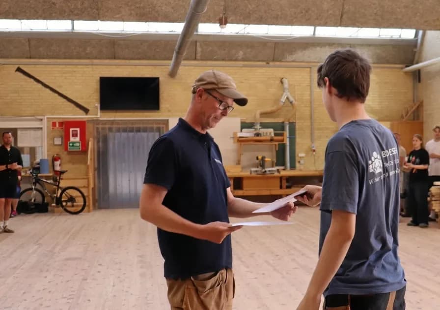 Man giving papers to young man in workshop