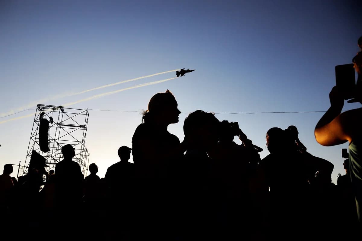 Silhouetted crowd watching a fighter jet in the sky