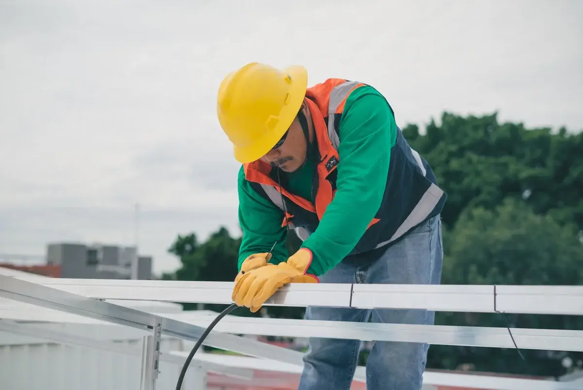 Construction worker with hard hat and gloves handling electrical cable on rooftop