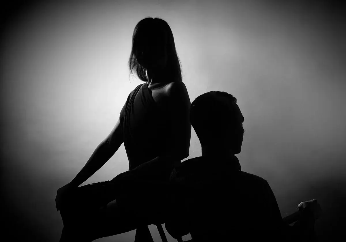 Silhouetted couple sitting back-to-back in a tense pose.