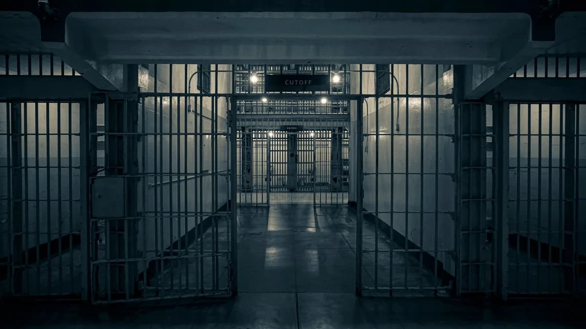 A dim prison corridor with barred gates and cell blocks.