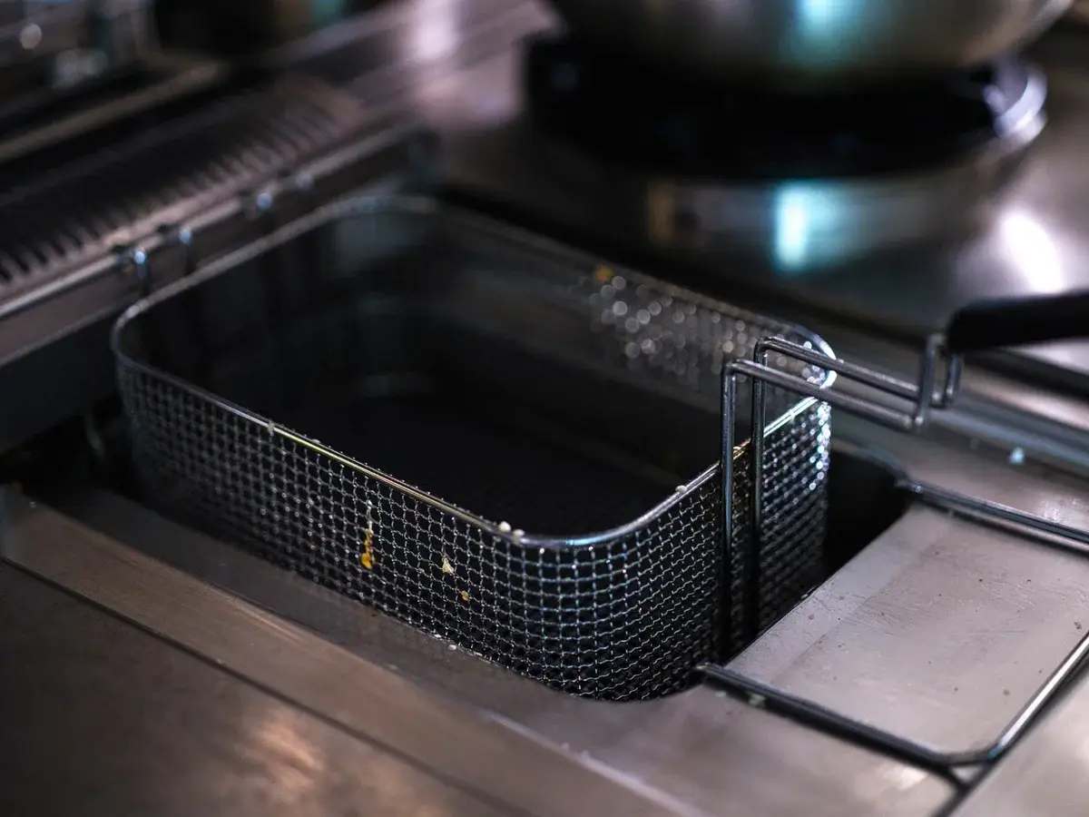 Empty fryer basket inside a stainless steel fryer