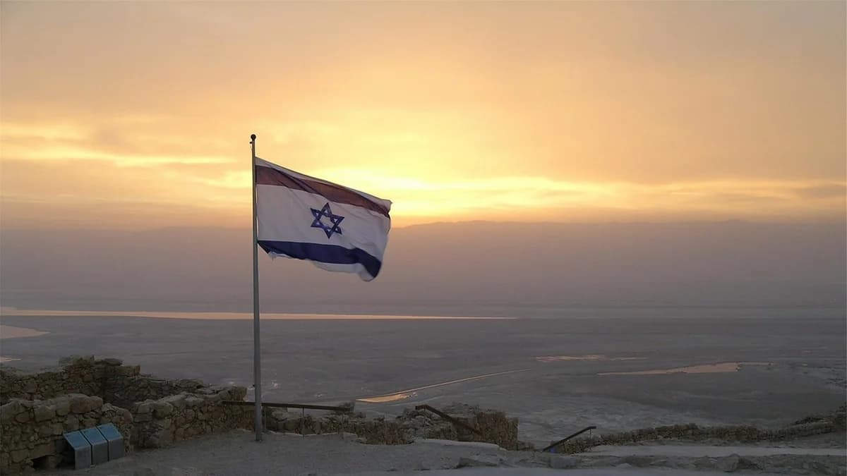 An Israeli flag flying at sunset over a landscape.