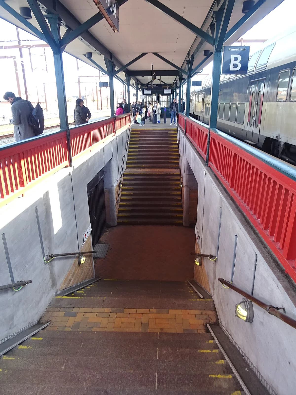 Stairs descending to a pedestrian tunnel at a train station platform.