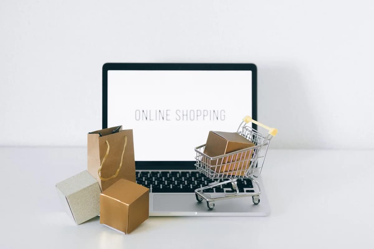 A laptop screen reading "ONLINE SHOPPING" with small packages and a shopping cart in front.