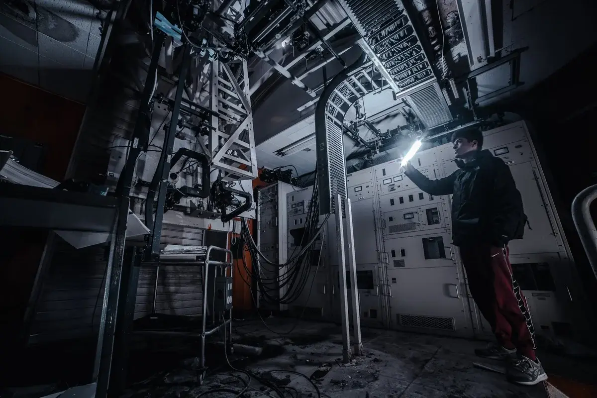 A technician shining a flashlight in a dark industrial control room.
